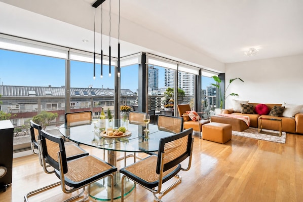 Un salón moderno con una mesa de comedor de vidrio, sofá de cuero y grandes ventanales con vistas a la ciudad.