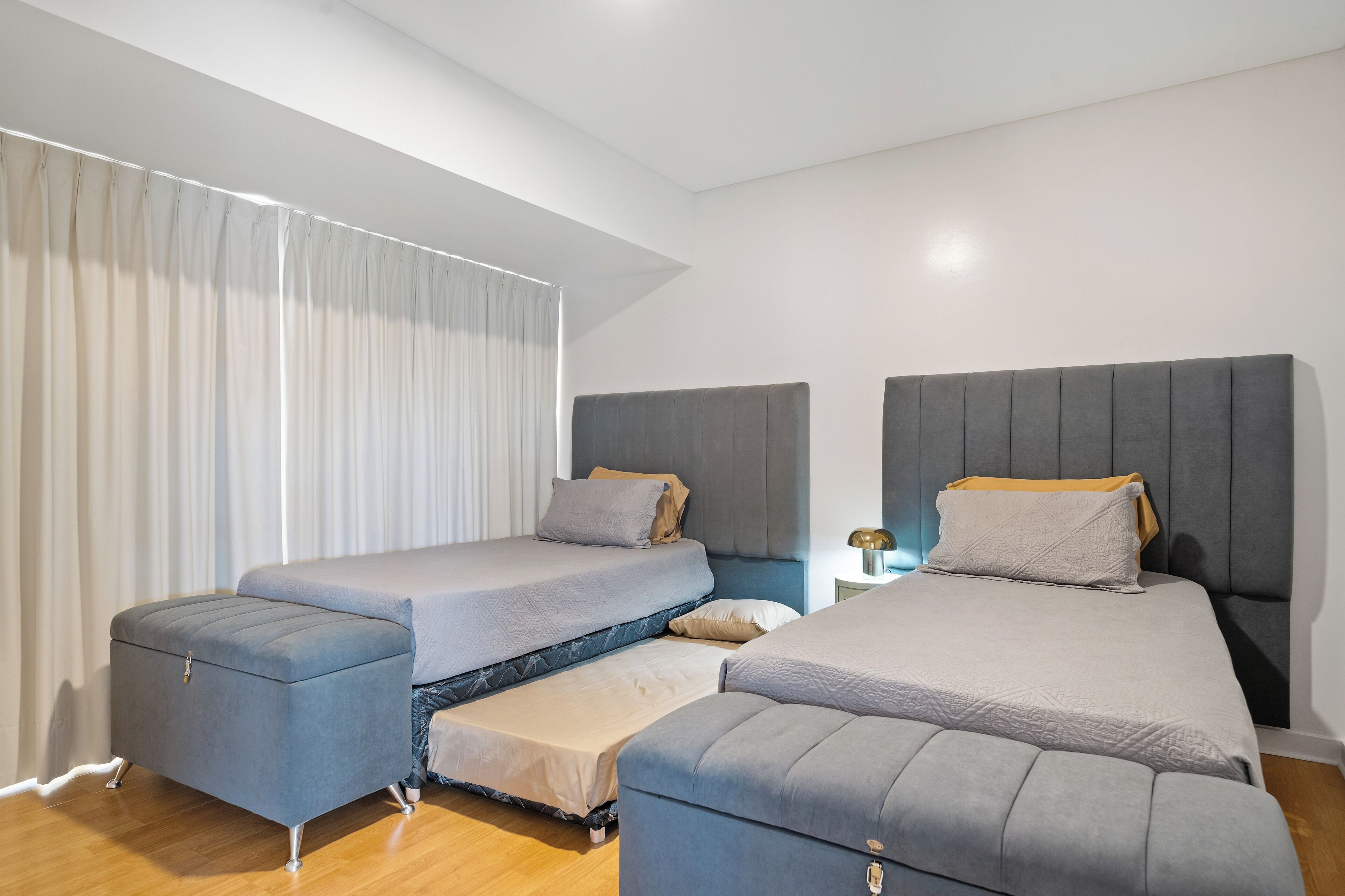 A modern bedroom with a large bed, two smaller beds, a nightstand, and a window with curtains.