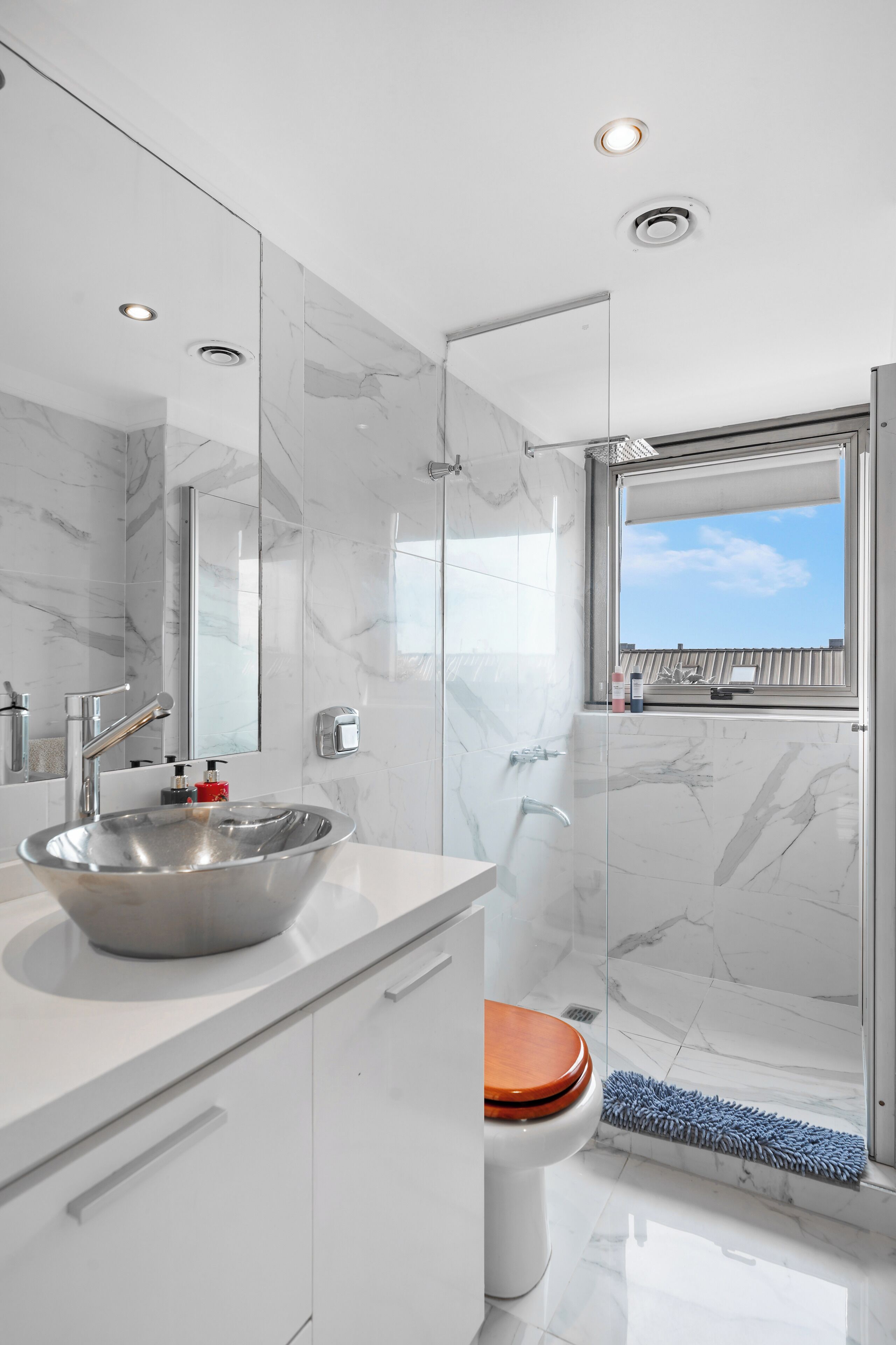 Ein modernes Badezimmer mit einer Duschkabine aus Glas, einem weißen Waschbecken mit Aufsatzbecken und einer Toilette mit Holzsitze.