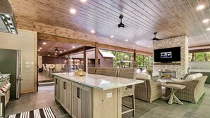 Cocina amplia con una isla grande, techo de madera y un televisor montado en una pared de piedra.