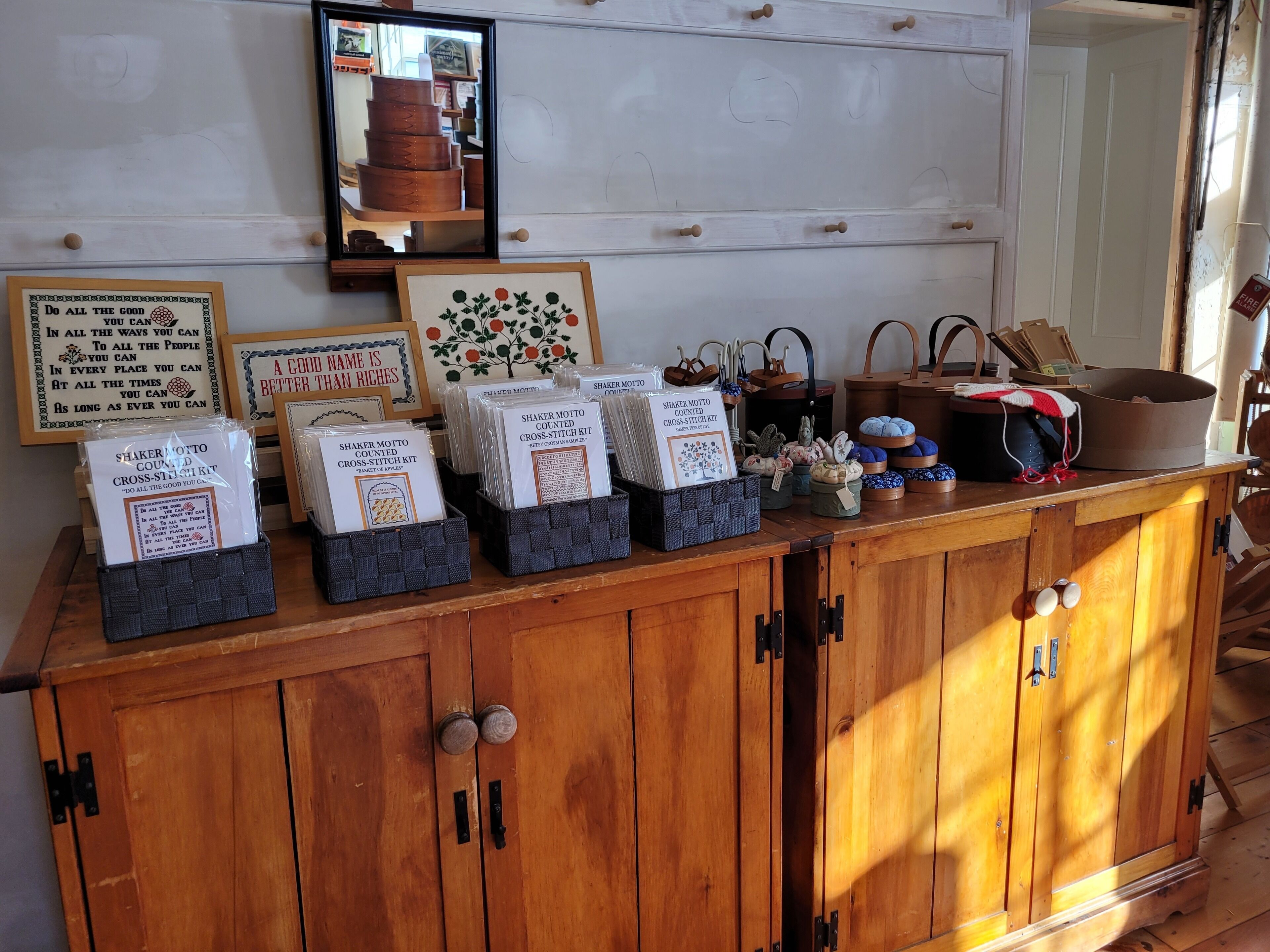 A wooden cabinet with drawers, a mirror, and various items including framed quotes and a cross-stitch kit.