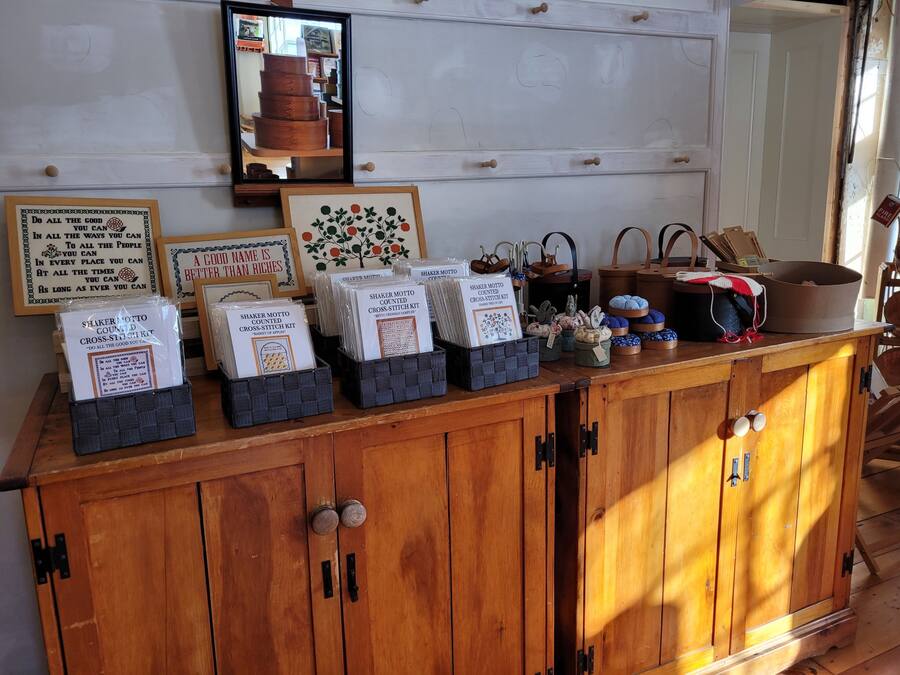 A wooden cabinet with drawers, a mirror, and various items including framed quotes and a cross-stitch kit.