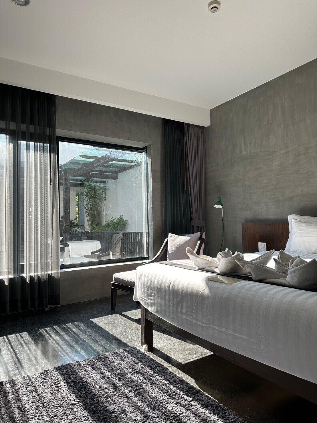 A modern hotel room with a large bed, a view of the outdoors, and a small table.