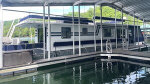 A covered dock with a boat, a small pool, and a view of greenery.
