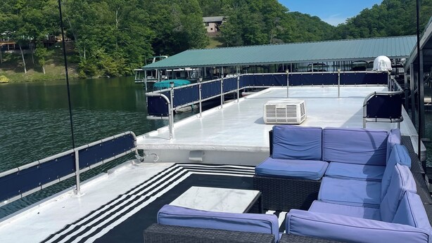 A boat deck with outdoor seating, a covered area, and a view of a forested area with a house in the background.