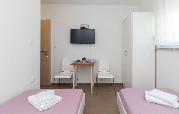 A small, clean room with two beds, a desk with chairs, a TV, and a wardrobe.