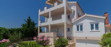 A two-story building with a balcony, a garage, and stone landscaping.