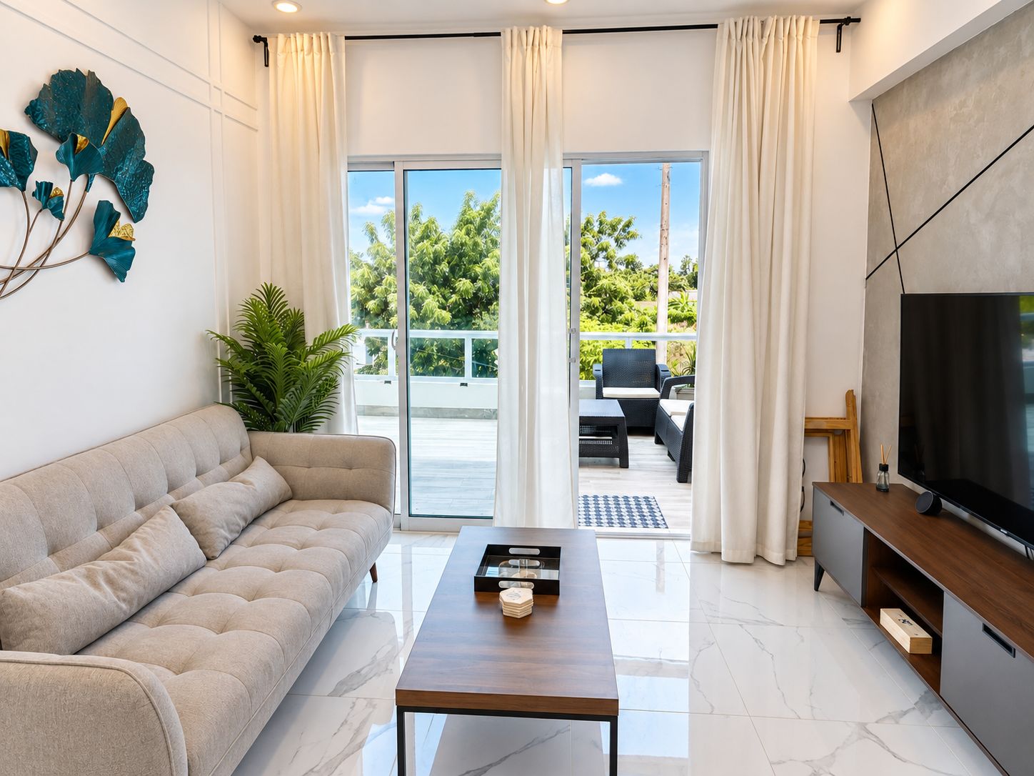 Un salon moderne comprenant un canapé, une table basse, un téléviseur et un balcon aménagé avec du mobilier d’extérieur.