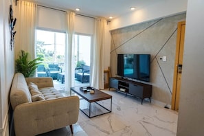 Uma sala de estar moderna com sofá, mesa de centro, televisão e vista através de grandes janelas.