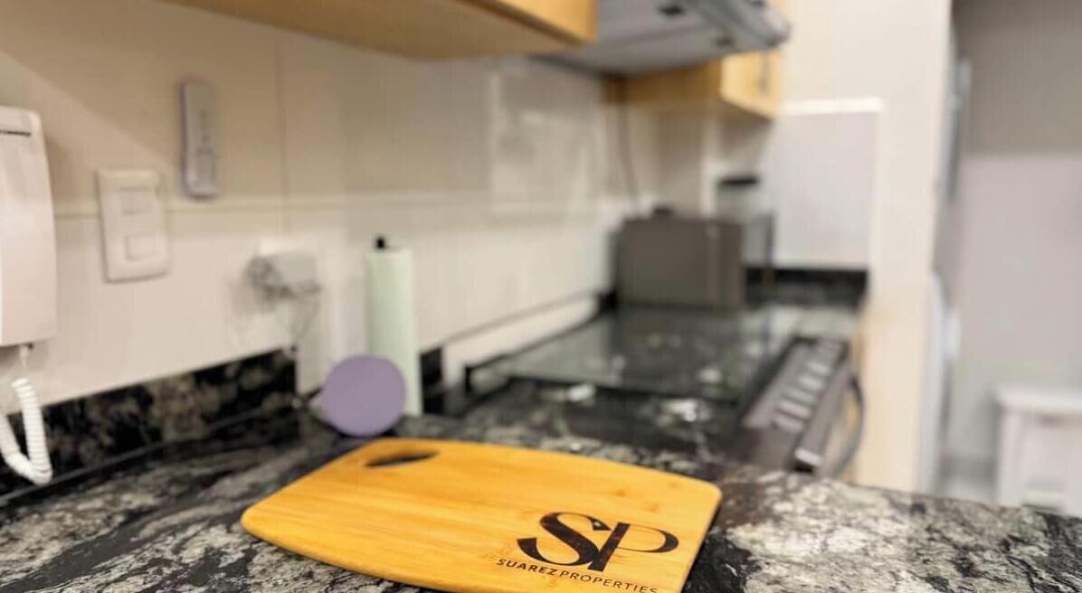 A kitchen with a wooden cutting board, a marble countertop, and a white tiled backsplash.