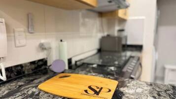 A kitchen with a wooden cutting board, a marble countertop, and a white tiled backsplash.
