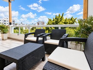 A balcony with wicker furniture, a view of buildings, and greenery.