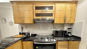 A kitchen with wooden cabinets, a gas stove, a microwave, and a coffee maker. - Tropico Smart by Suarez Properties | 2BR & Jacuzzi (Santo Domingo Este)