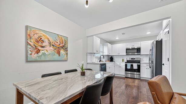 A modern kitchen with white cabinets, stainless steel appliances, and a marble dining table.