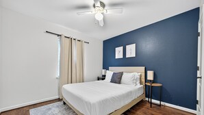 A bedroom with a bed, a ceiling fan, a nightstand, a lamp, and two framed pictures on the wall.