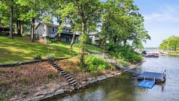 A riverside property with a dock, a wooden staircase leading to a house, and a boat docked in the water. - Lakefront Home on Grand Lake in Grove – Dock, 10 Beds, Game Room, Honey Creek (Grove)