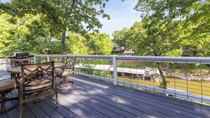 A wooden deck with outdoor furniture, overlooking a river with boats and a small dock. - Lakefront Home on Grand Lake in Grove – Dock, 10 Beds, Game Room, Honey Creek (Grove)