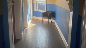 Un pasillo con pared azul y amarilla, una ventana y una silla.