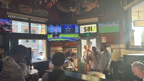 Un bar con varias pantallas mostrando eventos deportivos, una banda tocando en vivo y clientes sentados en mesas.