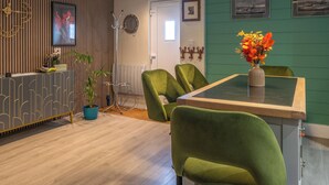 Un intérieur moderne avec un coin repas comprenant une chaise à revêtement vert, une table ornée d’un vase de fleurs et un comptoir d’accueil agrémenté d’une plante.