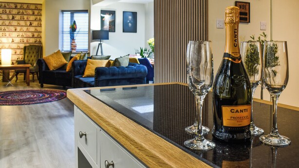 Un salon moderne avec un canapé bleu foncé, une table basse en bois et une bouteille de Canti Prosecco posée sur un comptoir noir.