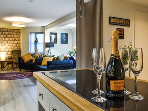 Uma sala de estar moderna com um sofá azul escuro, uma mesa de centro de madeira e uma garrafa de Canti Prosecco sobre uma bancada preta.