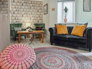 Uma sala de estar com poltrona verde, sofá preto com almofadas amarelas, mesa de centro de madeira e tapete estampado.