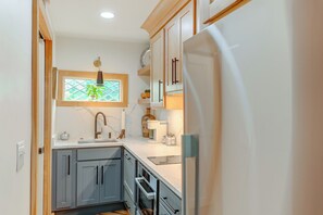 Una cocina compacta con armarios grises, horno integrado, refrigerador de acero inoxidable y una ventana con diseño geométrico.