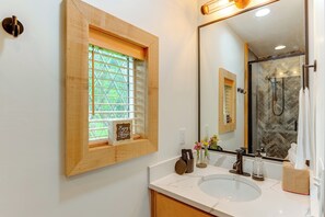 Un baño con un espejo grande, un lavamanos y una ventana con vistas a zonas verdes.