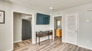 Una habitación con piso de madera, un escritorio con cubierta de vidrio, un espejo y una puerta blanca.