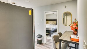 Una habitación de hotel compacta con kitchenette, un comedor con mesa y sillas, una cama con cabecera capitonada y un espejo en la pared.