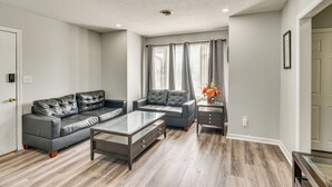 Una sala de estar con un sofá de cuero gris, una mesa de centro de vidrio y un sillón de dos plazas también gris.