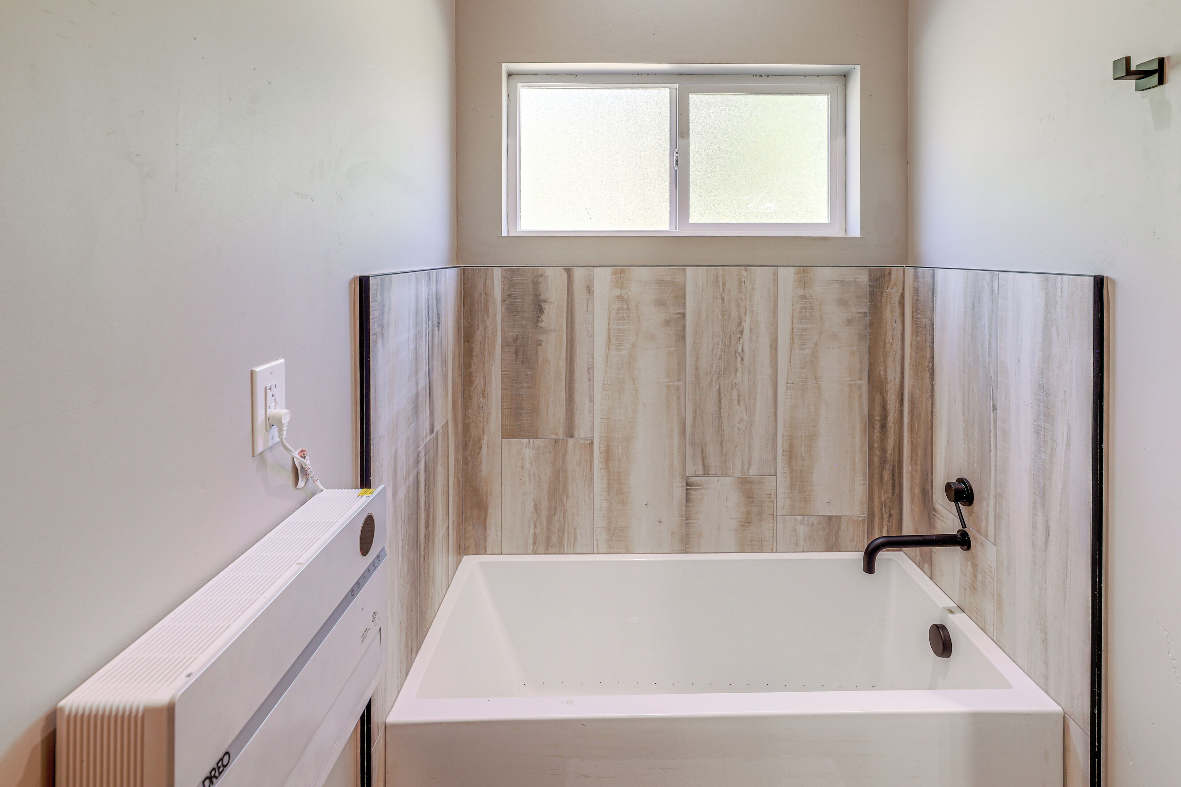 A modern bathroom with a bathtub, a window, and a wooden wall panel.