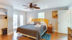 A bedroom with a bed, a ceiling fan, a nightstand, a lamp, a window, and a door. - Fish, Swim & More: Lakefront Retreat in Ocklawaha! (Ocklawaha)