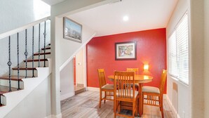 A dining area with a wooden table and chairs, a staircase with a railing, and a red wall with a framed picture. - Fish, Swim & More: Lakefront Retreat in Ocklawaha! (Ocklawaha)
