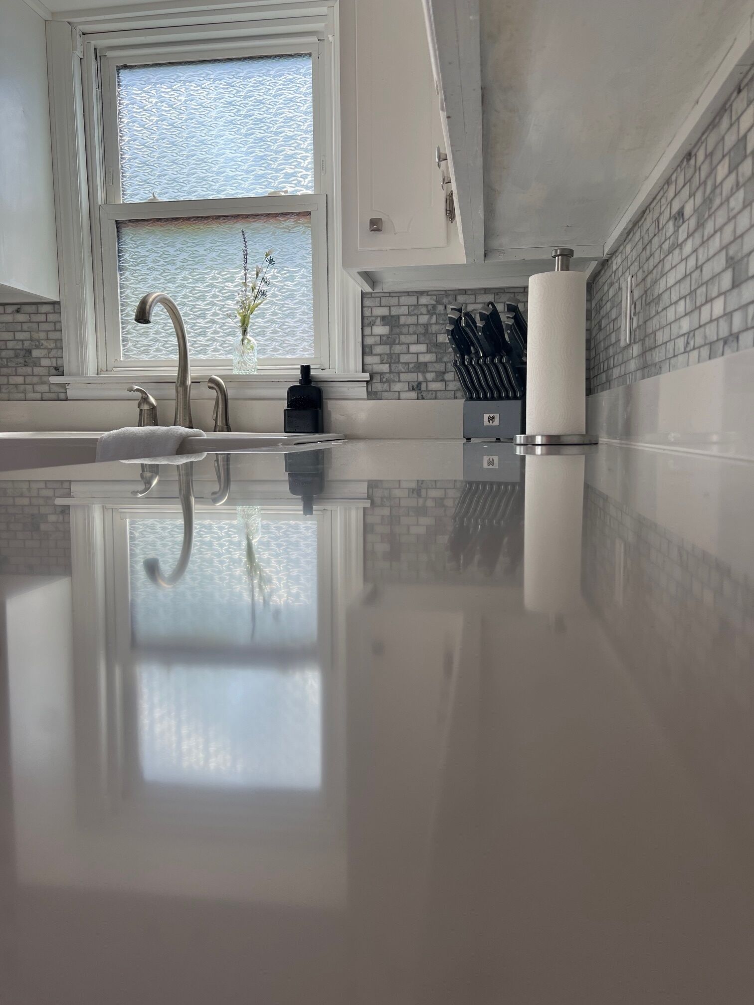 Een moderne keuken met een groot raam, een roestvrijstalen spoelbak en een achterwand van baksteen.