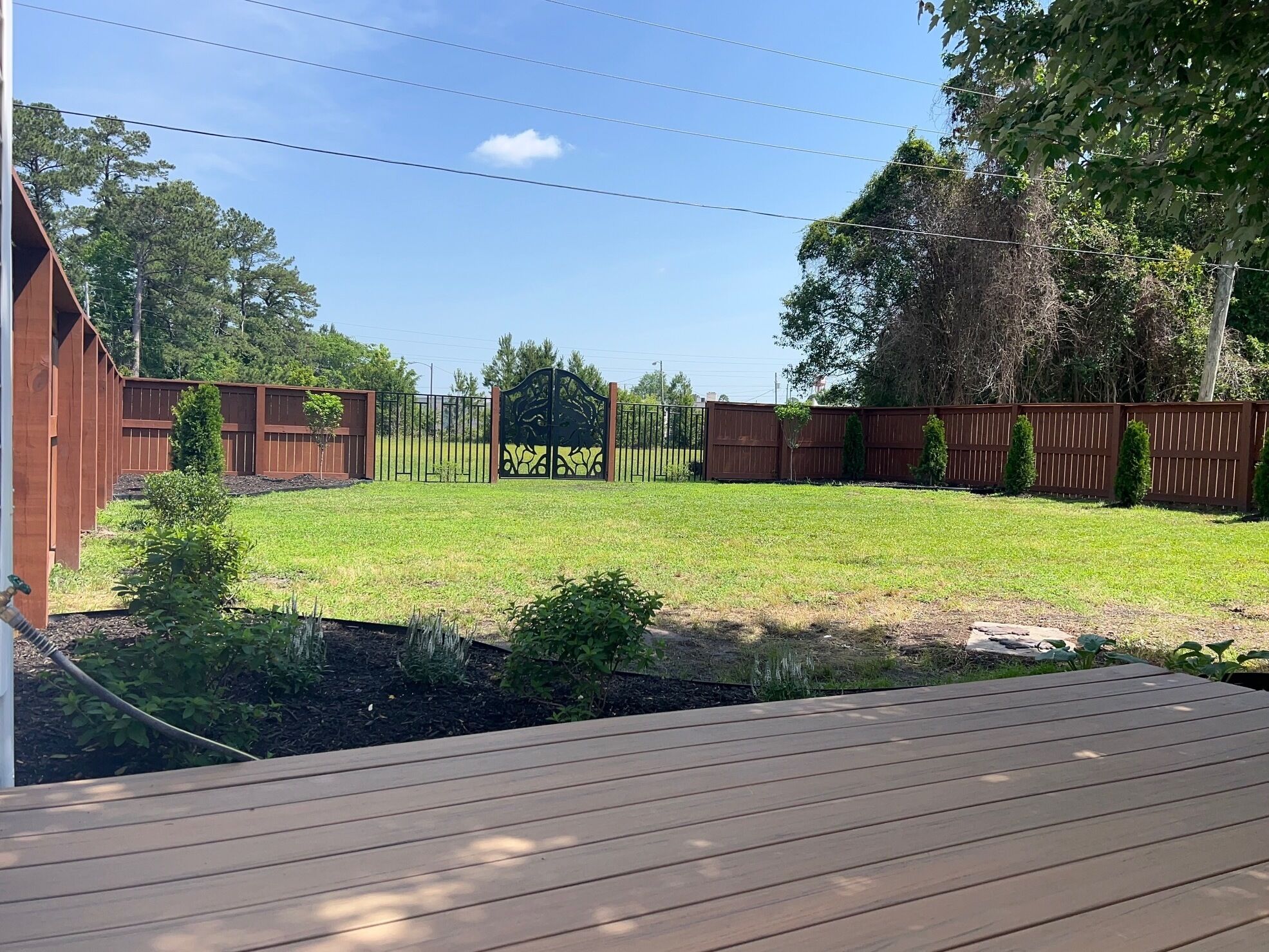 A backyard with a wooden deck, a fenced area, and a grassy lawn.