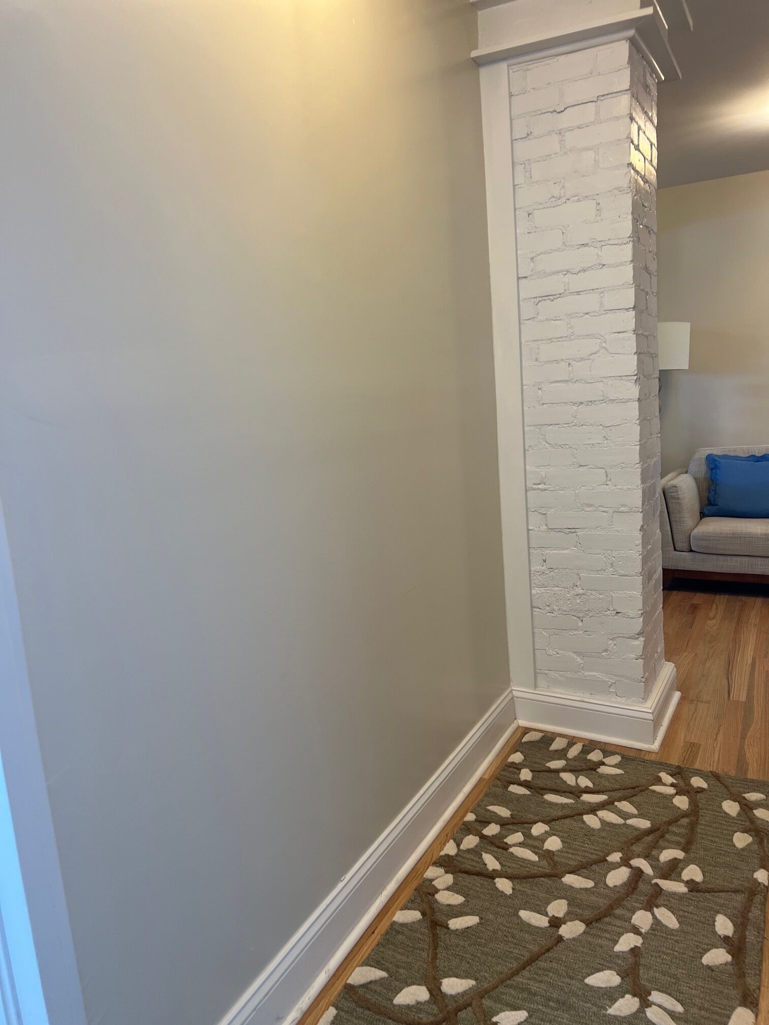 Ein Flur mit einer Wand aus weißen Ziegelsteinen, Holzboden und einem gemusterten Teppich.