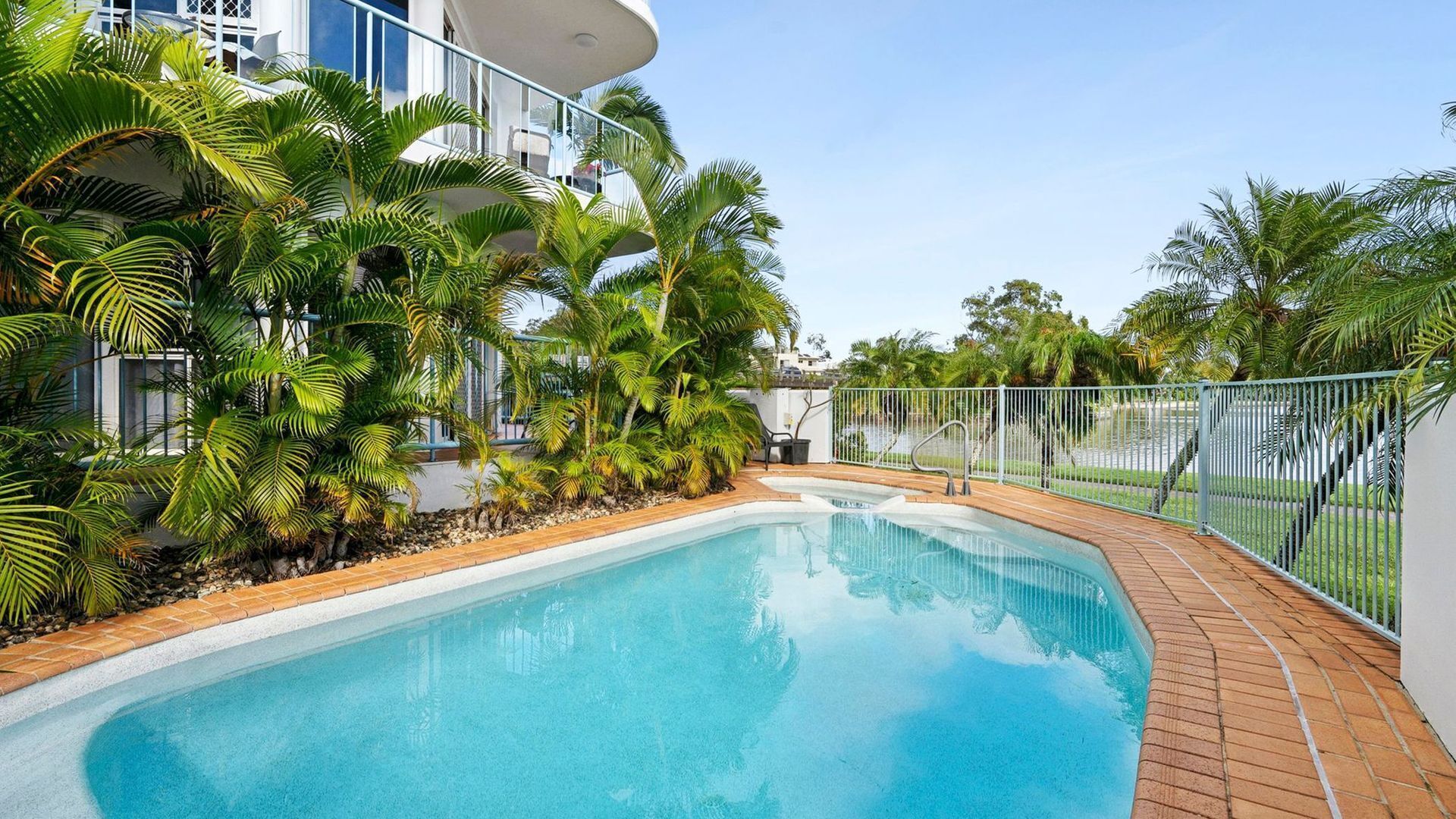 A swimming pool surrounded by palm trees and a white building with balconies.