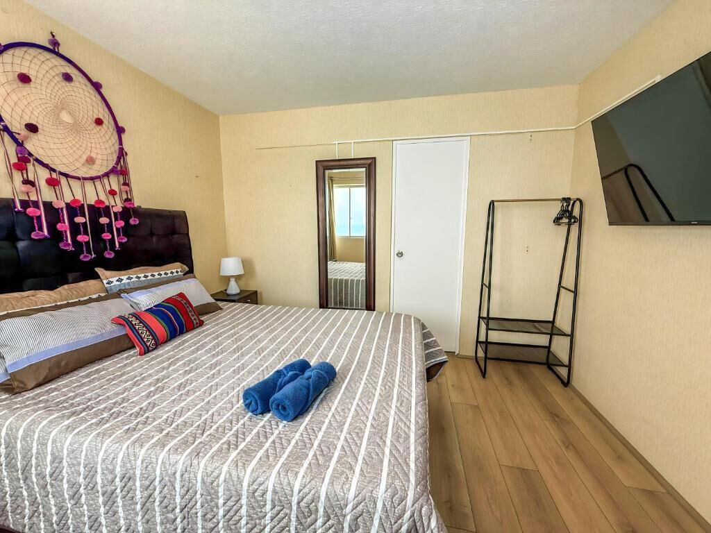 Ein Hotelzimmer mit einem Bett, einem an der Wand befestigten Fernseher, einer Tür und einem kleinen Tisch mit einer Lampe.
