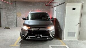 A car parked in a parking garage with concrete walls, a door marked "D-03", and a yellow line on the floor.
