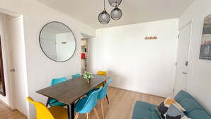A dining area with a wooden table, blue and yellow chairs, a round mirror, and a hanging light fixture.