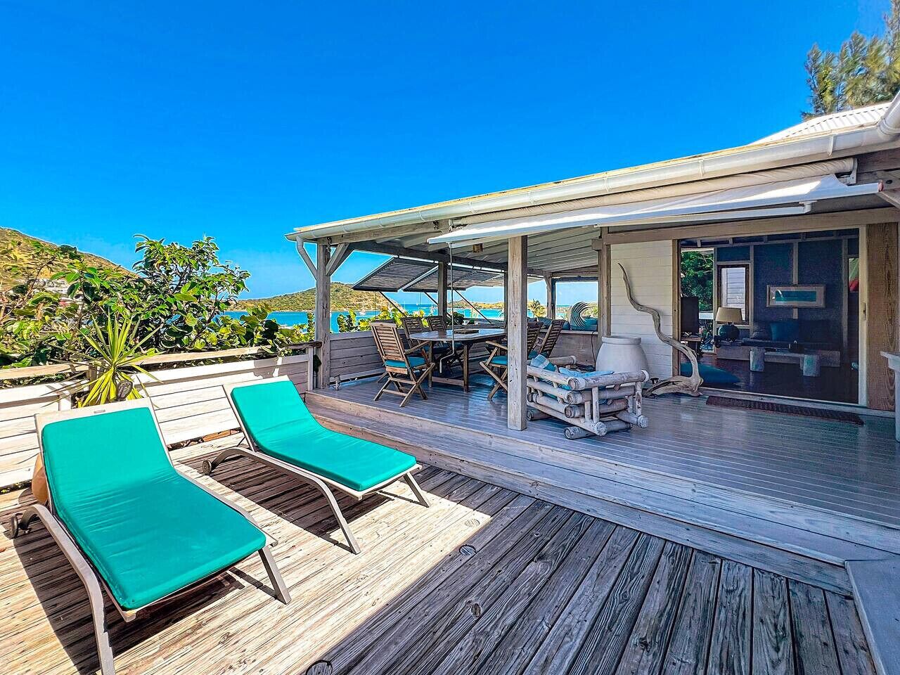 A wooden deck with two green lounge chairs, a covered outdoor dining area, and a view of the ocean.