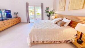 A spacious bedroom with a large bed, wooden headboard, and a nightstand with a lamp. - Villa Côté Sable, Accès plage, Vue mer, Elégance (Orient Bay)