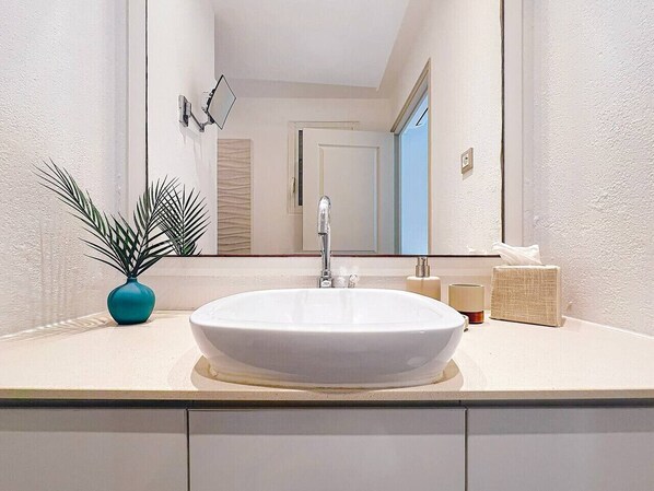 Een badkamer met een witte wastafel, een spiegel, een zeepdispenser en een potplant.
