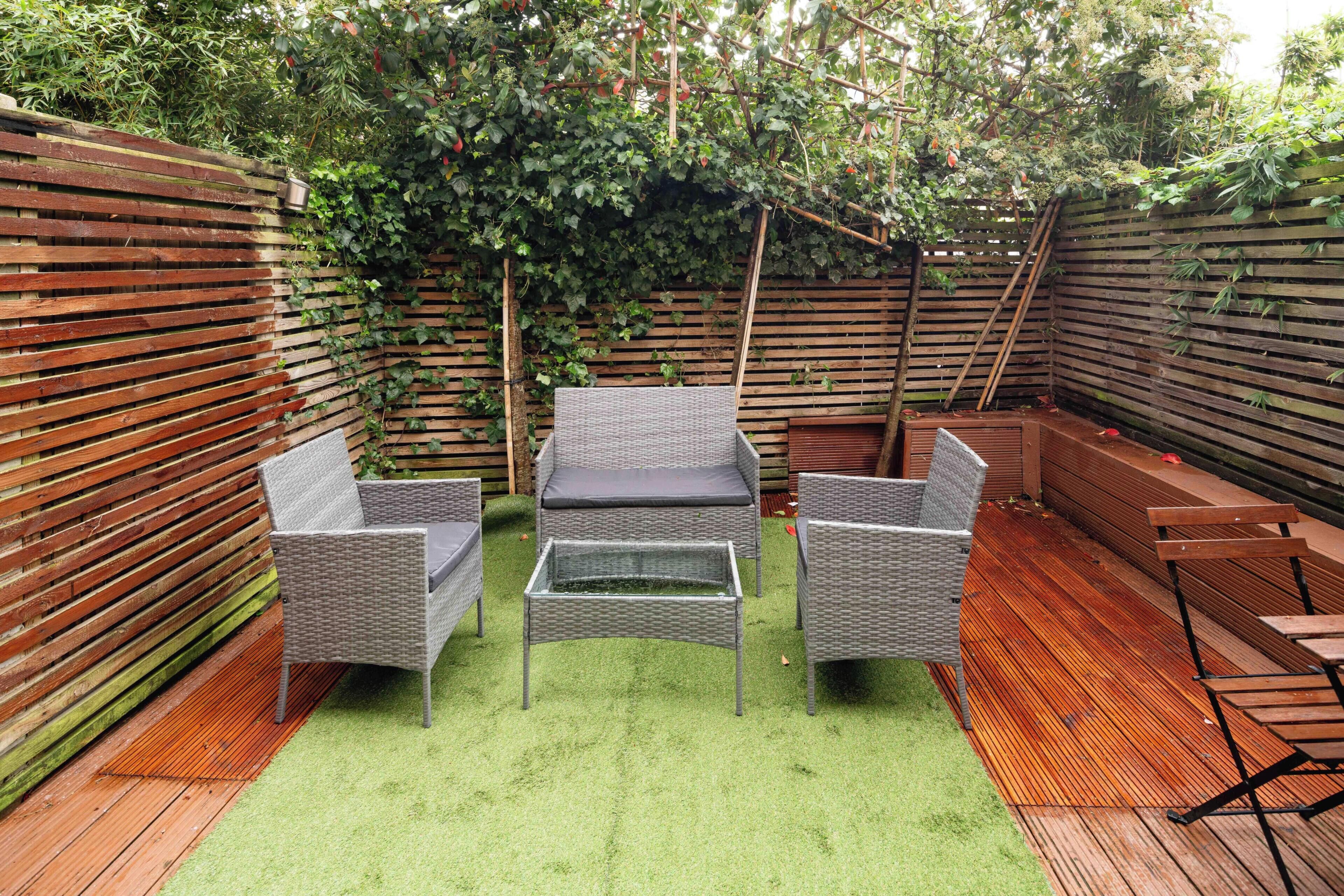 A patio with wicker furniture, a glass-top table, and a wooden deck.
