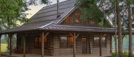 A rustic log cabin with a metal roof, wooden porch, and a 'Welcome' sign.