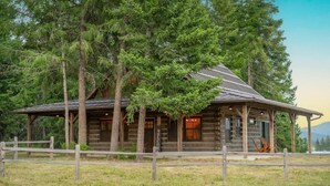 Ein rustikales Blockhaus mit einladendem Eingang, umgeben von hohen Bäumen und einem Holzzaun.