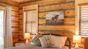 Ein Schlafzimmer einer Blockhütte mit einem Bett, zwei Nachttischlampen, einem Sessel, einem Teppich und einem Deckenventilator.