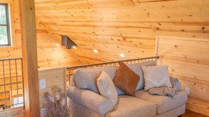 Ein gemütliches Zimmer mit Holzbalkendecke, einem grauen Sofa mit Kissen und einem Blumentopf.